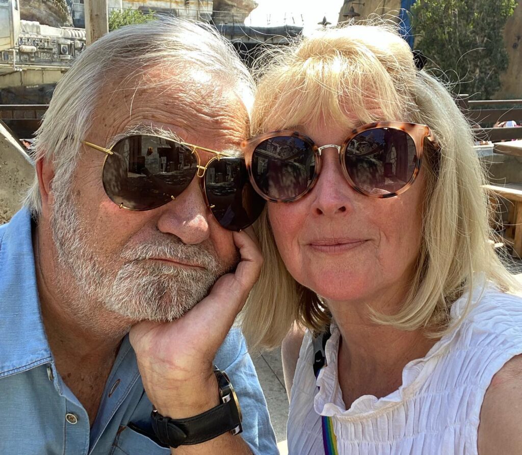 john mccook leaning his head on his palm wearing sunglasses, with wife laurette Spang