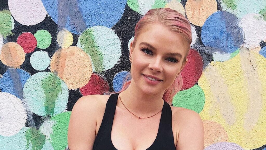 kelli goss wearing a black tanktop standing in front of a colorful background