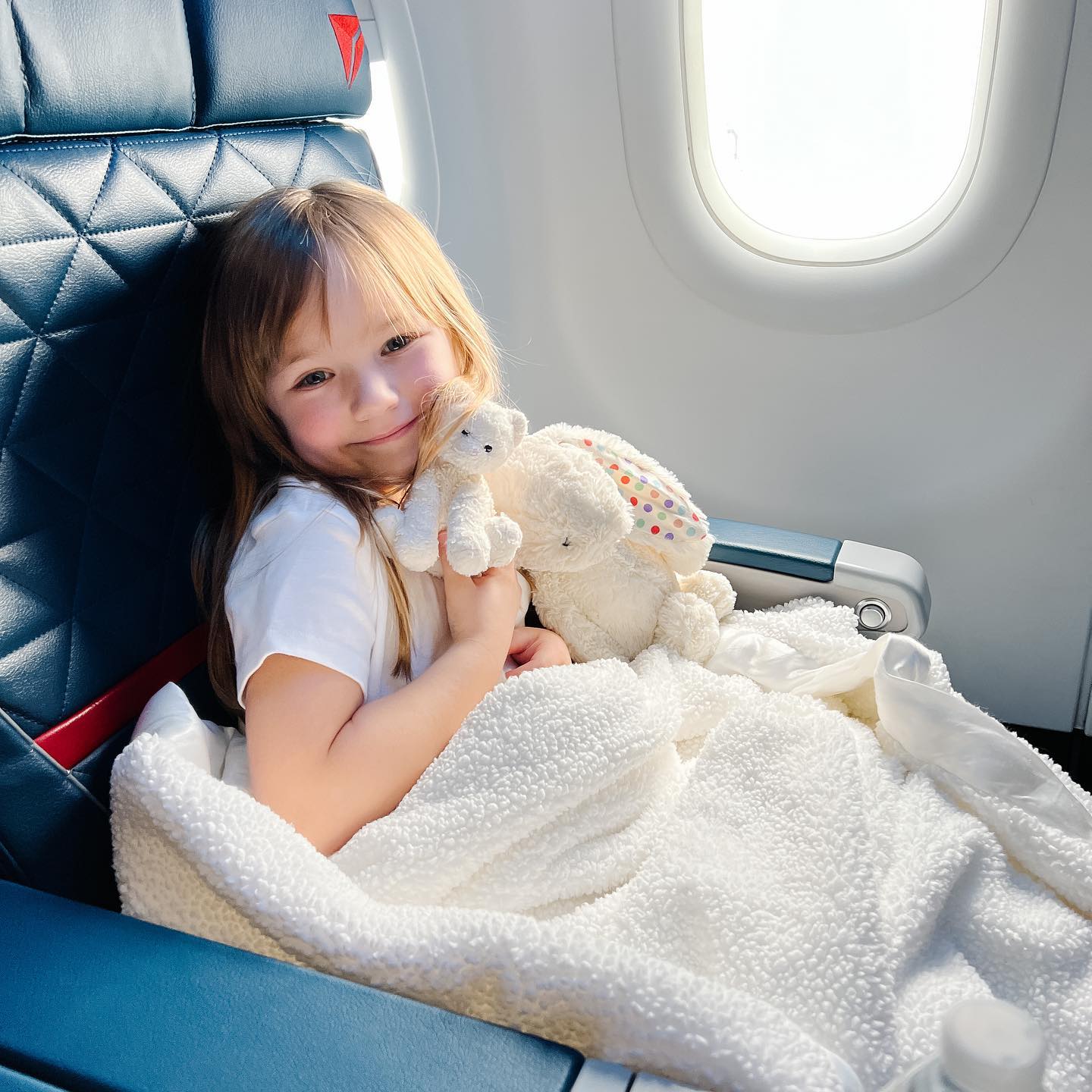 Remington Evans holding a teddy bear in sitting on an airplane seat