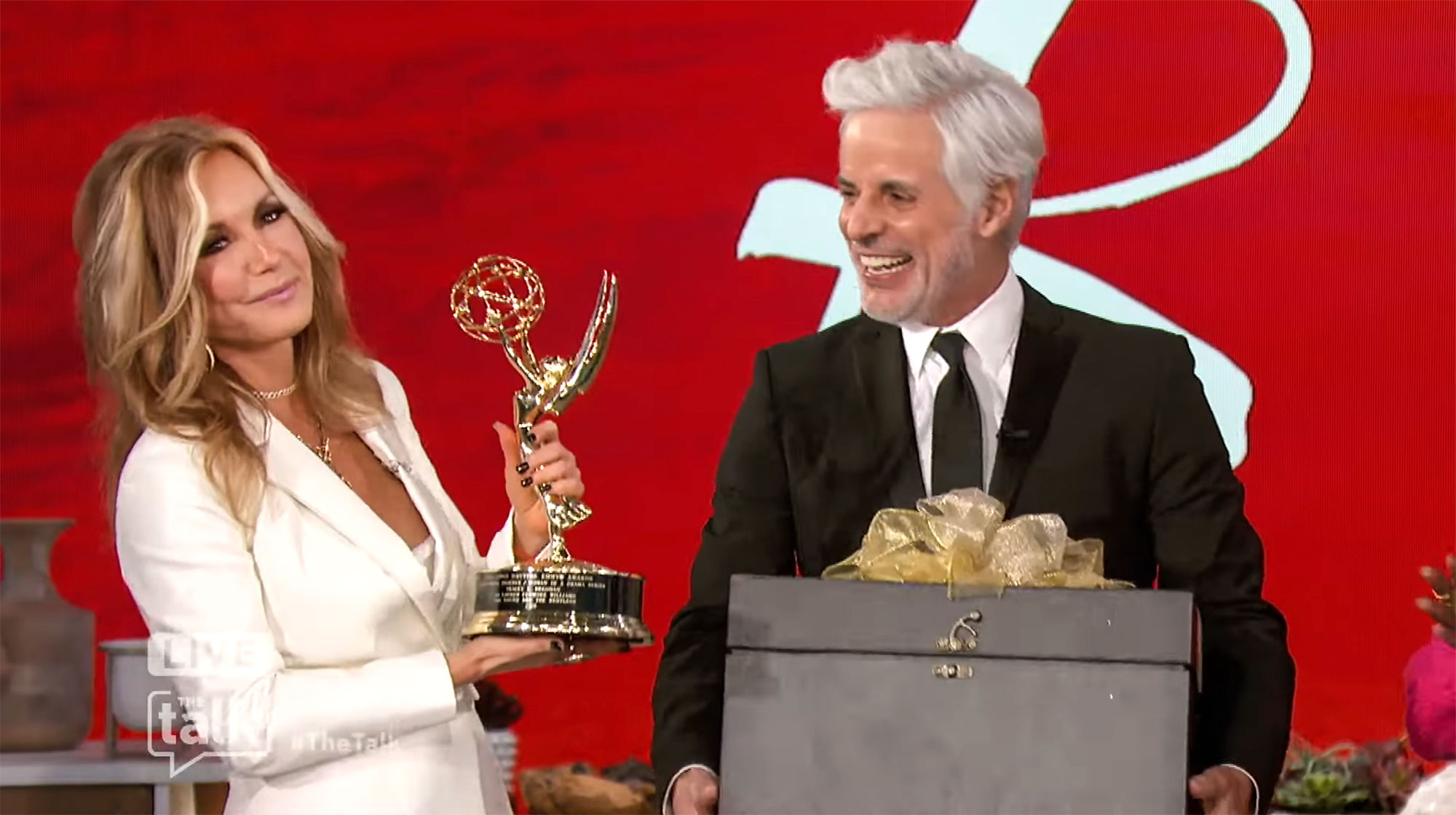 Tracey E Bregman holding her new Emmy Award beside Christian LeBlanc who's holding a big black gift box