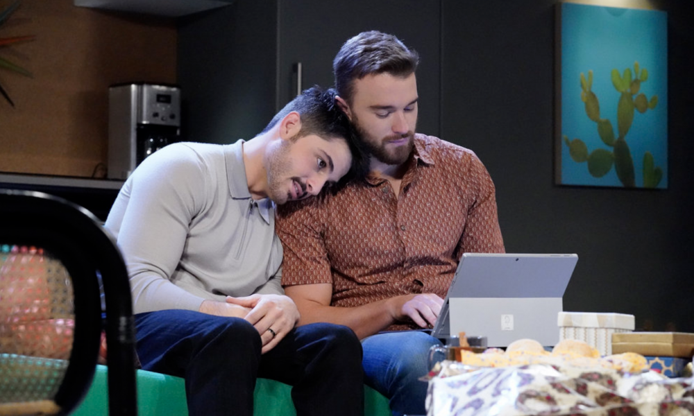 Zach Tinker laying down on Chandler Massey's shoulder while he's busy with an electronic. 